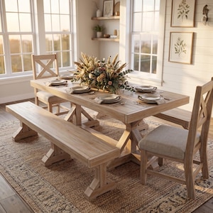 May include: A light-colored wooden dining table set with a bench and chairs. The table is set with plates and silverware, and a floral arrangement sits in the center. The room has large windows and a neutral rug.