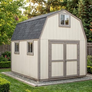 Può includere: Un piccolo capannone in stile fienile, color crema, con tetto grigio scuro e finiture grigie. Il capannone ha due finestre e doppie porte. È posto su una base di ghiaia ed è circondato da un prato verde e da giardini.