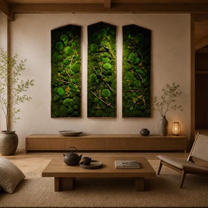 Op de afbeelding: Een moderne woonkamer met een minimalistisch ontwerp. Drie verticale moskunstwerken hangen aan de muur. Een houten console en een lage salontafel zijn aanwezig. Een theepot en dienblad staan op de tafel. Een beige tapijt en een houten stoel.