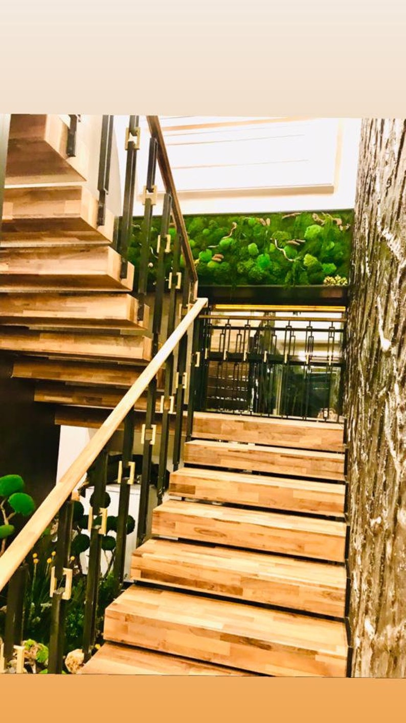 May include: A wooden staircase with a black metal railing and gold accents. The staircase leads up to a green moss wall.