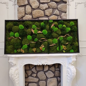 May include: A framed moss wall art piece with a black frame and a variety of green moss textures. The moss is arranged in a natural, organic pattern with some dried grasses and branches.