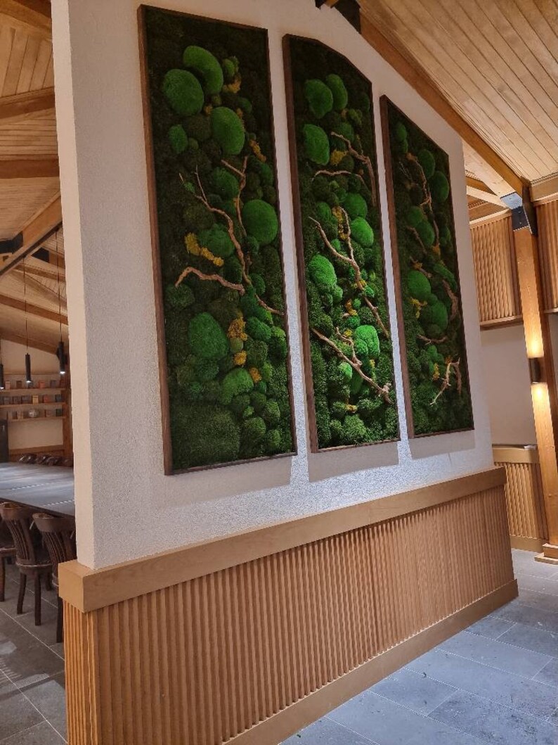 Op de afbeelding: Drie verticale wandkunstwerken met bewaard groen mos en takken in houten frames. De moskunst voegt een natuurlijk, gestructureerd element toe aan het interieur. De frames zijn warmbruin en complementeren het groene mos.