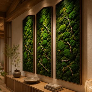 Op de afbeelding: Drie ingelijste verticale wandkunstwerken met levendig groen mos en delicate takken. Het kunstwerk is geplaatst tegen een neutrale muur, met daaronder een houten console, wat een natuurlijke en serene esthetiek cre&euml;ert. De frames hebben een donkerbruine afwerking.