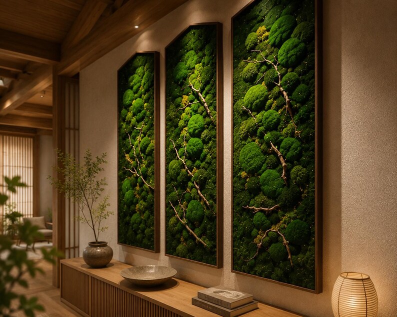 Op de afbeelding: Drie ingelijste verticale wandkunstwerken met levendig groen mos en delicate takken. Het kunstwerk is geplaatst tegen een neutrale muur, met daaronder een houten console, wat een natuurlijke en serene esthetiek cre&euml;ert. De frames hebben een donkerbruine afwerking.