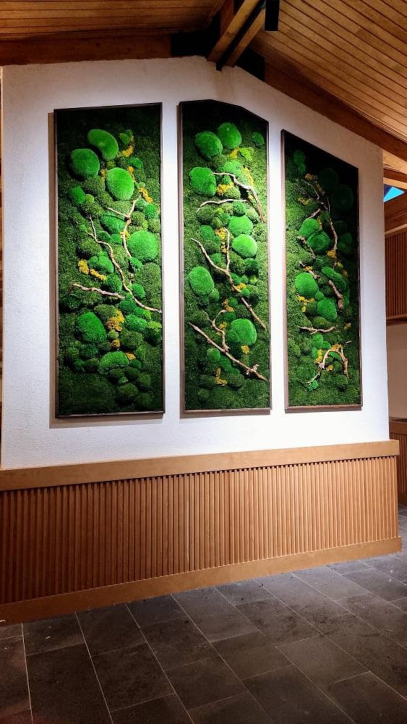 Op de afbeelding: Drie ingelijste verticale wandkunstwerken met levendig groen mos en droge takken. De moskunst heeft een natuurlijke, organische esthetiek, met een mix van texturen en groentinten. De frames hebben een neutrale kleur, als aanvulling op het kunstwerk.
