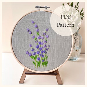 Pode incluir: Um padrão PDF para bordar um buquê de flores de lavanda em um aro. O bordado é feito em um tecido de linho cinza.