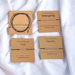 May include: Four cards with black string bracelets on them. Each card has a different message in Morse code: "keep going", "beautiful badas", "I Can", and "Fearless". Each card has the text "Morse Code Bracelet" and "Handmade Item".
