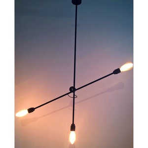 May include: A black metal ceiling light fixture with three light bulbs. The light fixture is in the shape of a cross with three arms extending from a central point.