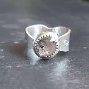 May include: A silver ring with a round, clear stone set in a starburst design. The stone has black inclusions.