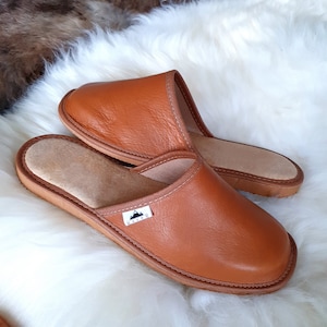 May include: A pair of brown leather slippers with a suede lining. The slippers have a simple design and are perfect for relaxing at home.