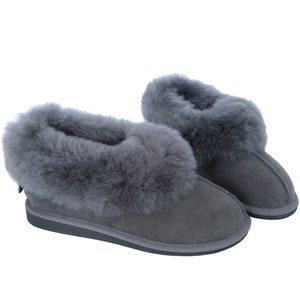 May include: A pair of grey sheepskin slippers with a fluffy lining. The slippers have a suede upper and a rubber sole.