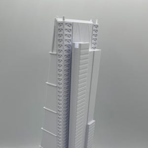 May include: A white architectural model of a tall skyscraper. The model has intricate details, including multiple windows and structural supports. The building is a light gray color and stands on a white base.
