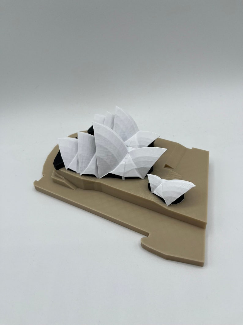 May include: A white 3D printed model of the Sydney Opera House on a brown base.