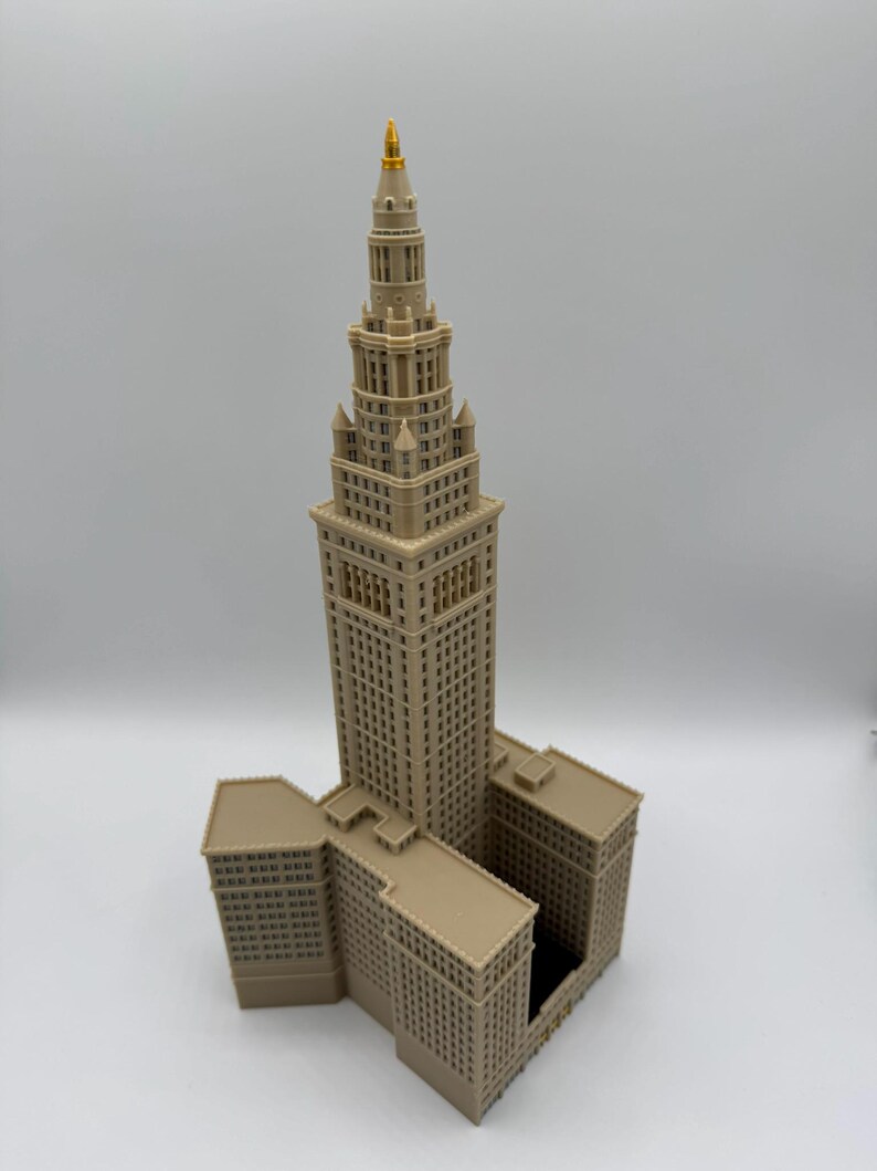 May include: A detailed model of a skyscraper with a tan exterior and a gold-colored spire. The building has multiple levels and architectural details, including windows and decorative elements. The model is a representation of a famous building.