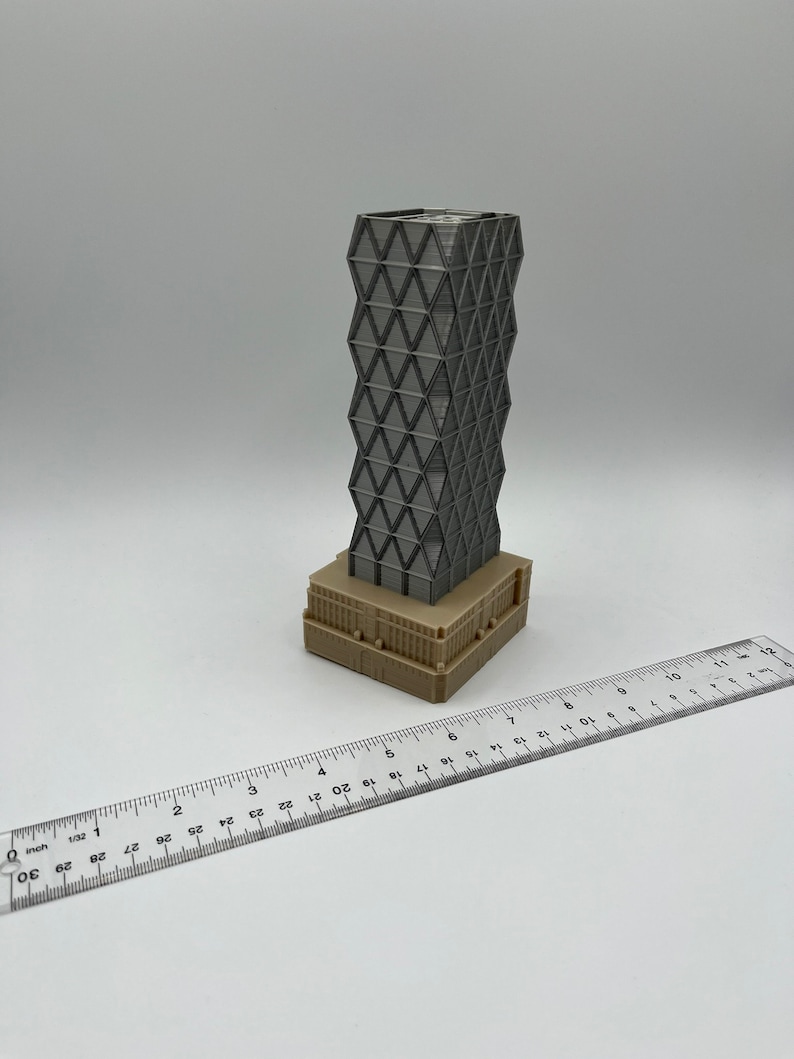 May include: A 3D printed model of a modern skyscraper with a geometric facade. The building is grey and has a brown base. The model is approximately 10 cm tall.