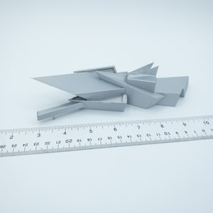 May include: A 3D printed model of a modern building with a geometric design. The model is made of a light gray plastic and is about 7 inches long.