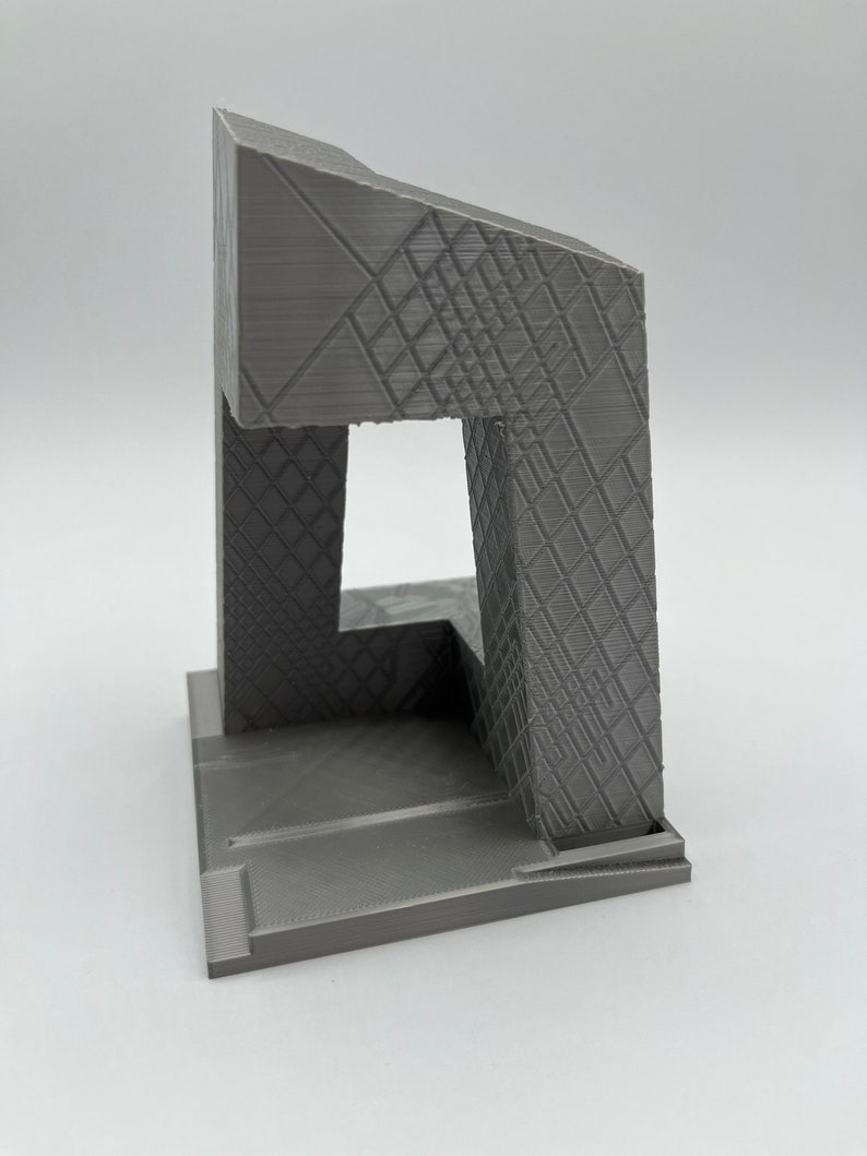 Peut inclure: Mod&egrave;le 3D imprim&eacute; en gris d'un b&acirc;timent avec un design g&eacute;om&eacute;trique. Le b&acirc;timent a une base carr&eacute;e et une haute tour rectangulaire avec une grande ouverture &agrave; l'avant. La tour est surmont&eacute;e d'un toit inclin&eacute;.