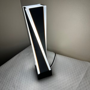 May include: A modern black and white table lamp with a geometric design. The lamp has a white base and a black shade with white lines.