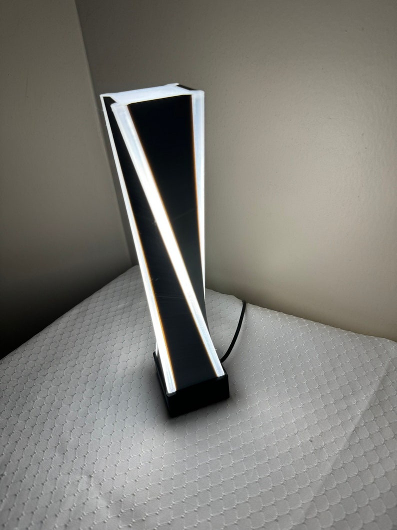 May include: A modern black and white table lamp with a geometric design. The lamp has a white base and a black shade with white lines.