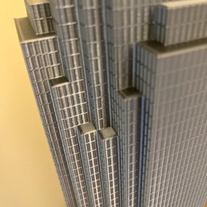 May include: A close-up of a gray, detailed model of a skyscraper. The model is made of stacked layers of small, rectangular pieces, creating a textured, geometric pattern.