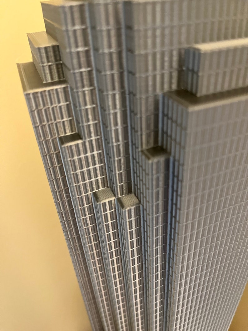 May include: A close-up of a gray, detailed model of a skyscraper. The model is made of stacked layers of small, rectangular pieces, creating a textured, geometric pattern.
