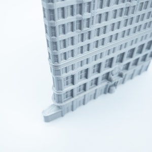 Puede incluir: Un modelo 3D impreso en gris de un edificio alto con muchas ventanas. El edificio tiene una fachada detallada y est&aacute; inclinado para mostrar el lado.