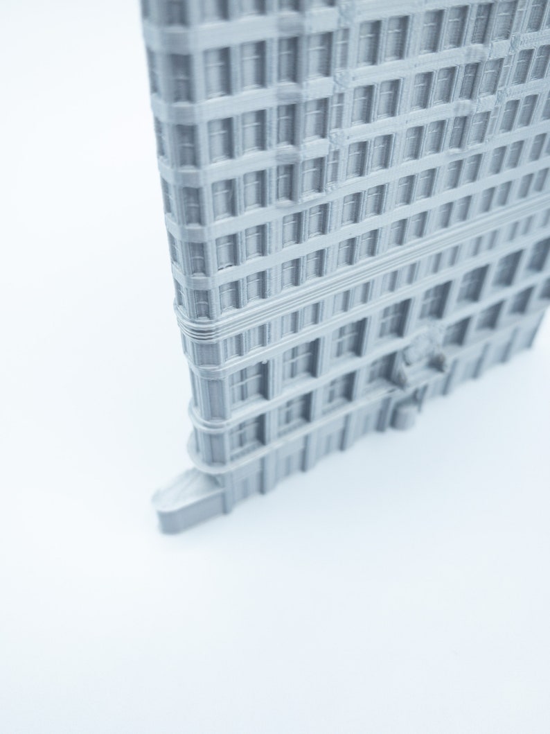 Puede incluir: Un modelo 3D impreso en gris de un edificio alto con muchas ventanas. El edificio tiene una fachada detallada y est&aacute; inclinado para mostrar el lado.
