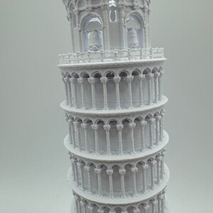 May include: A white 3D printed model of the Leaning Tower of Pisa. The model is detailed with arches and columns, and has a textured surface.