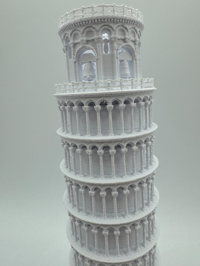 May include: A white 3D printed model of the Leaning Tower of Pisa. The model is detailed with arches and columns, and has a textured surface.