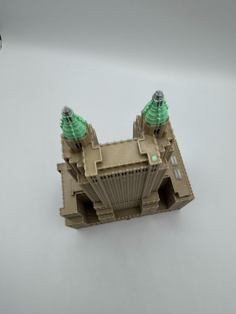 Może przedstawiać: Szczeg&oacute;łowy model miniaturowy wieżowca, z fasadą w kolorze beżowym i wieżami zwieńczonymi zielenią. Model prezentuje detale architektoniczne, w tym okna i elementy dekoracyjne, na białym tle.