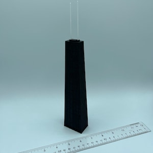 May include: A black architectural model of a skyscraper with two clear antennas. A ruler is placed next to the model. The model is approximately 10 inches tall.
