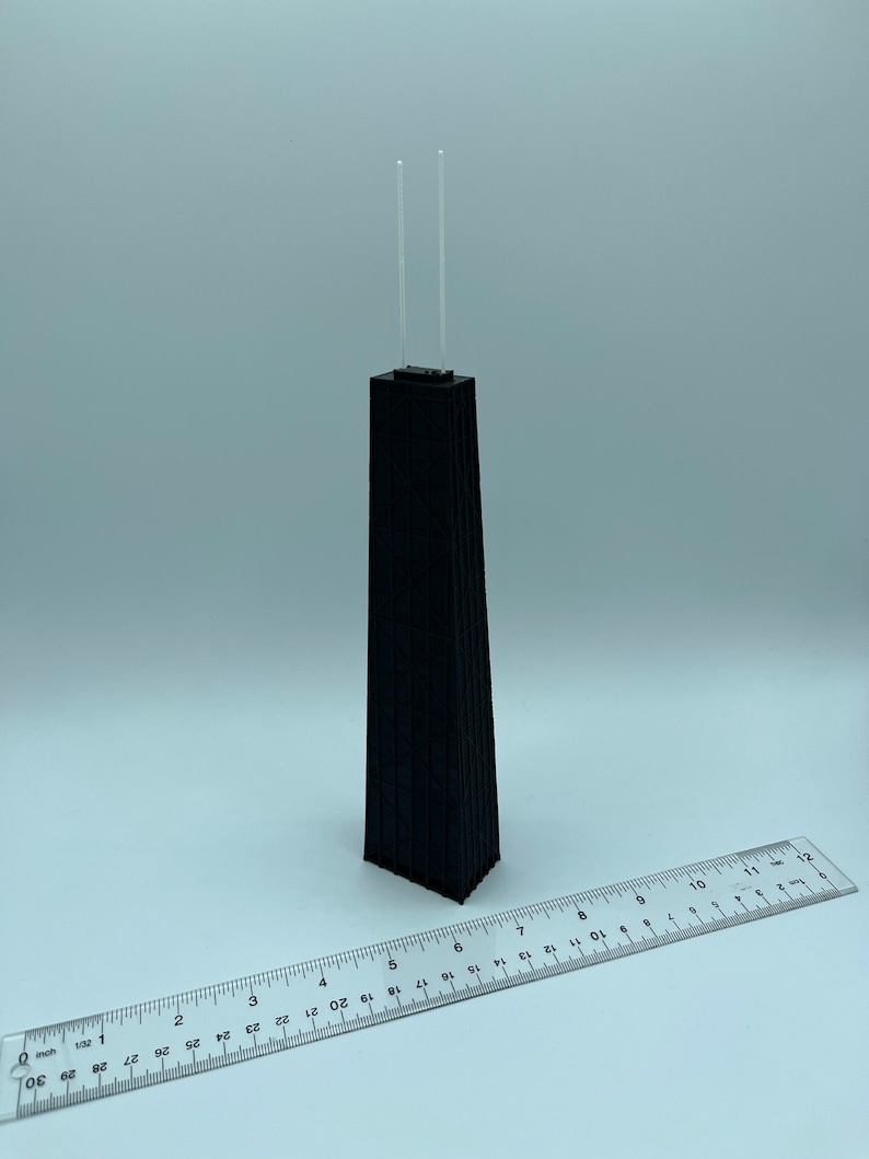 May include: A black architectural model of a skyscraper with two clear antennas. A ruler is placed next to the model. The model is approximately 10 inches tall.