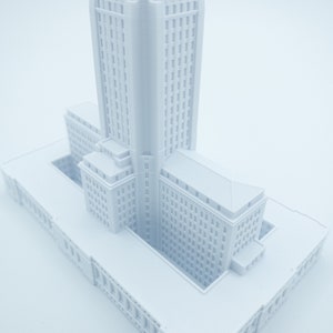 May include: A white 3D printed model of a tall building with a square base and a central courtyard.