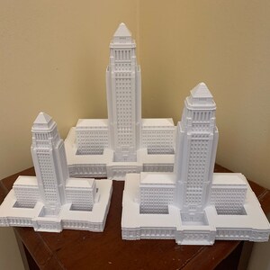 May include: Three white 3D printed models of the Los Angeles City Hall building, each at a different scale.
