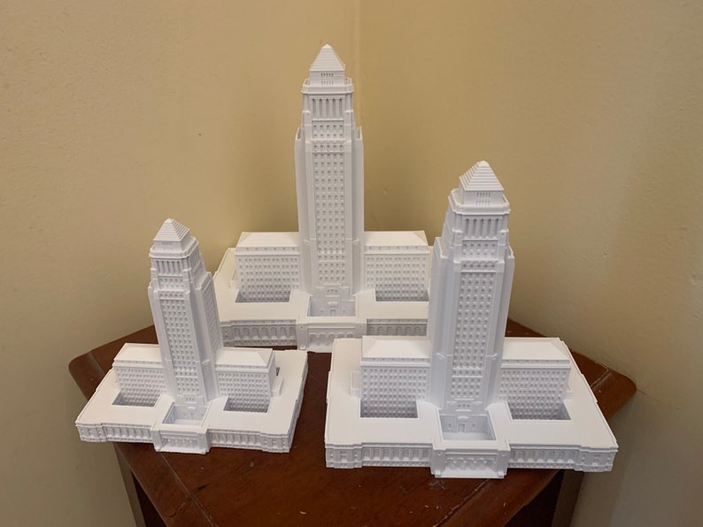 May include: Three white 3D printed models of the Los Angeles City Hall building, each at a different scale.