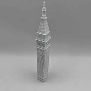 May include: A white 3D printed model of a tall building with a pointed roof and many windows.
