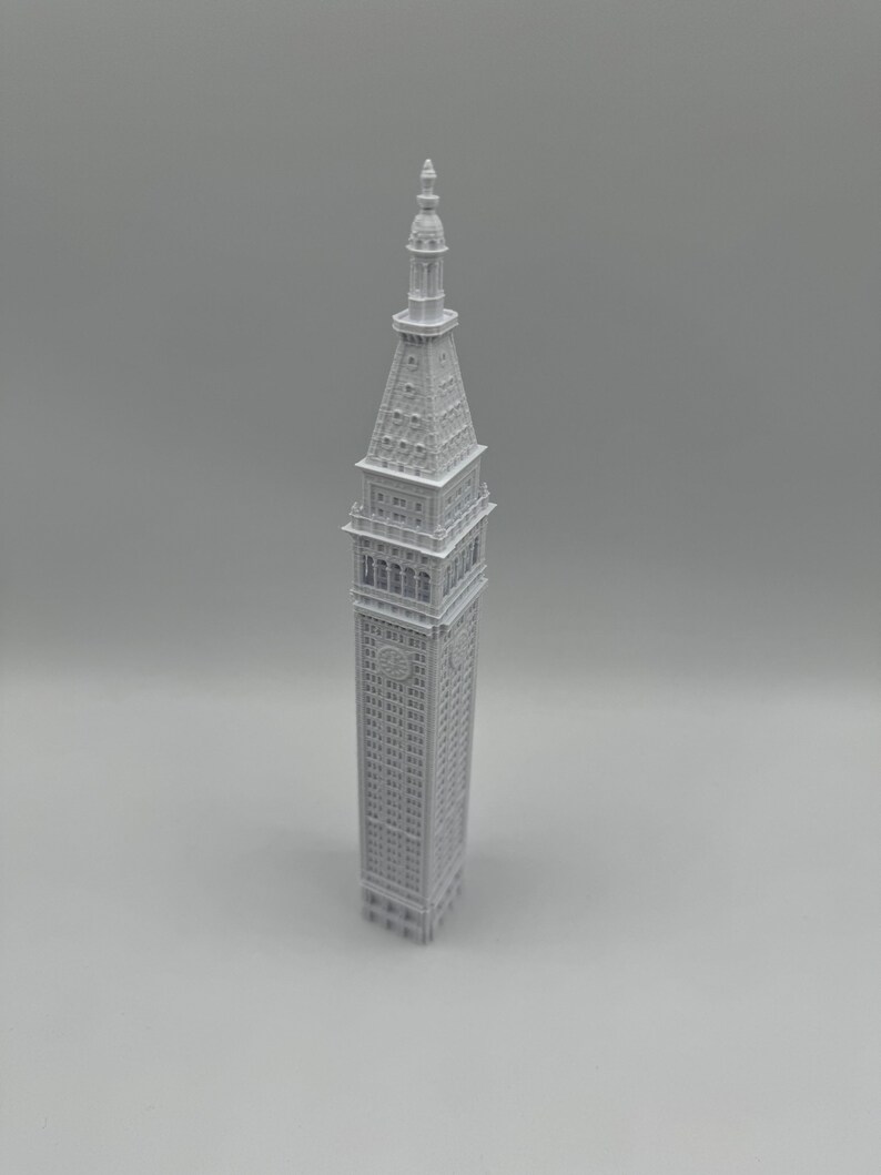 May include: A white 3D printed model of a tall building with a pointed roof and many windows.