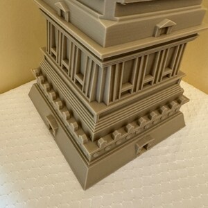 May include: A 3D printed model of a multi-level structure with a square base and a pointed top. The model is made of a light brown plastic and has intricate details, including columns, arches, and a decorative border.