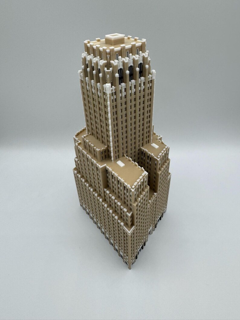 May include: A detailed model of a skyscraper, with a tan exterior and white detailing. The building has a tiered design, with a rectangular base and a tall, slender tower. The model is set against a plain white background.