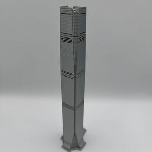 May include: A gray miniature skyscraper model with a rectangular design. The building has horizontal lines and a detailed facade. The base of the model has a star-like shape. The model is a representation of a modern architectural design.
