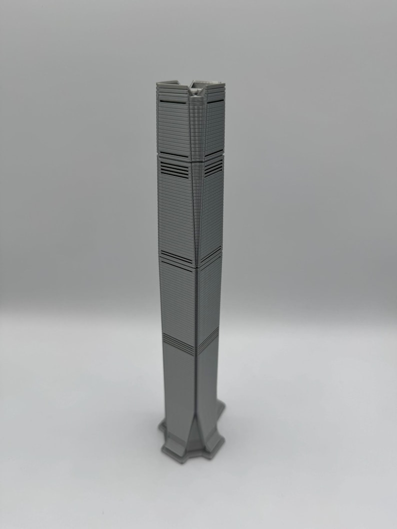 May include: A gray miniature skyscraper model with a rectangular design. The building has horizontal lines and a detailed facade. The base of the model has a star-like shape. The model is a representation of a modern architectural design.