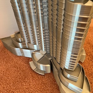 May include: A detailed 3D printed model of a modern skyscraper with a unique, curved design. The model is made of grey plastic and features intricate details, including balconies and windows.