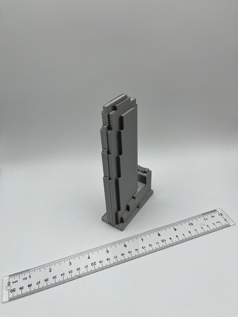 May include: A gray 3D printed model of a skyscraper building. The model is about 7 inches tall and is sitting on a white surface. A ruler is in the foreground.