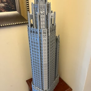 May include: A detailed 3D printed model of a skyscraper with a grey finish. The model is on a wooden table.