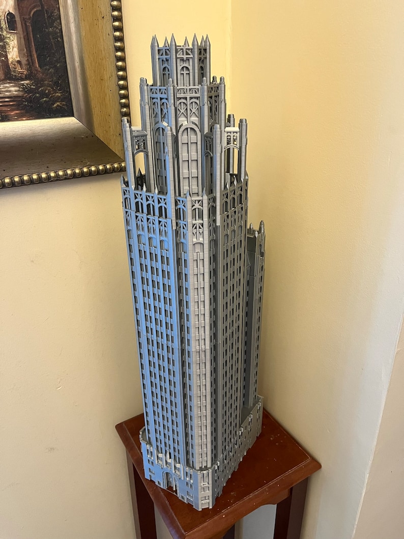 May include: A detailed 3D printed model of a skyscraper with a grey finish. The model is on a wooden table.