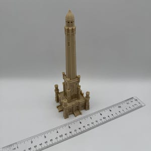 May include: A beige model of a tall tower with a detailed architectural design, featuring a domed top and multiple levels. A ruler is placed next to the model, showing measurements in inches.