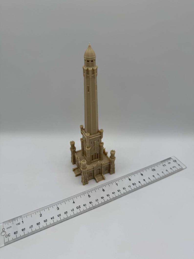 May include: A beige model of a tall tower with a detailed architectural design, featuring a domed top and multiple levels. A ruler is placed next to the model, showing measurements in inches.