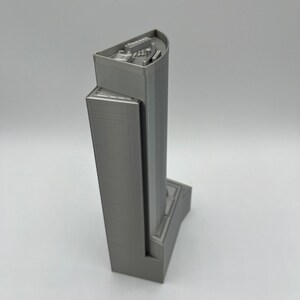 May include: A gray 3D printed model of a skyscraper with a detailed top and a base.