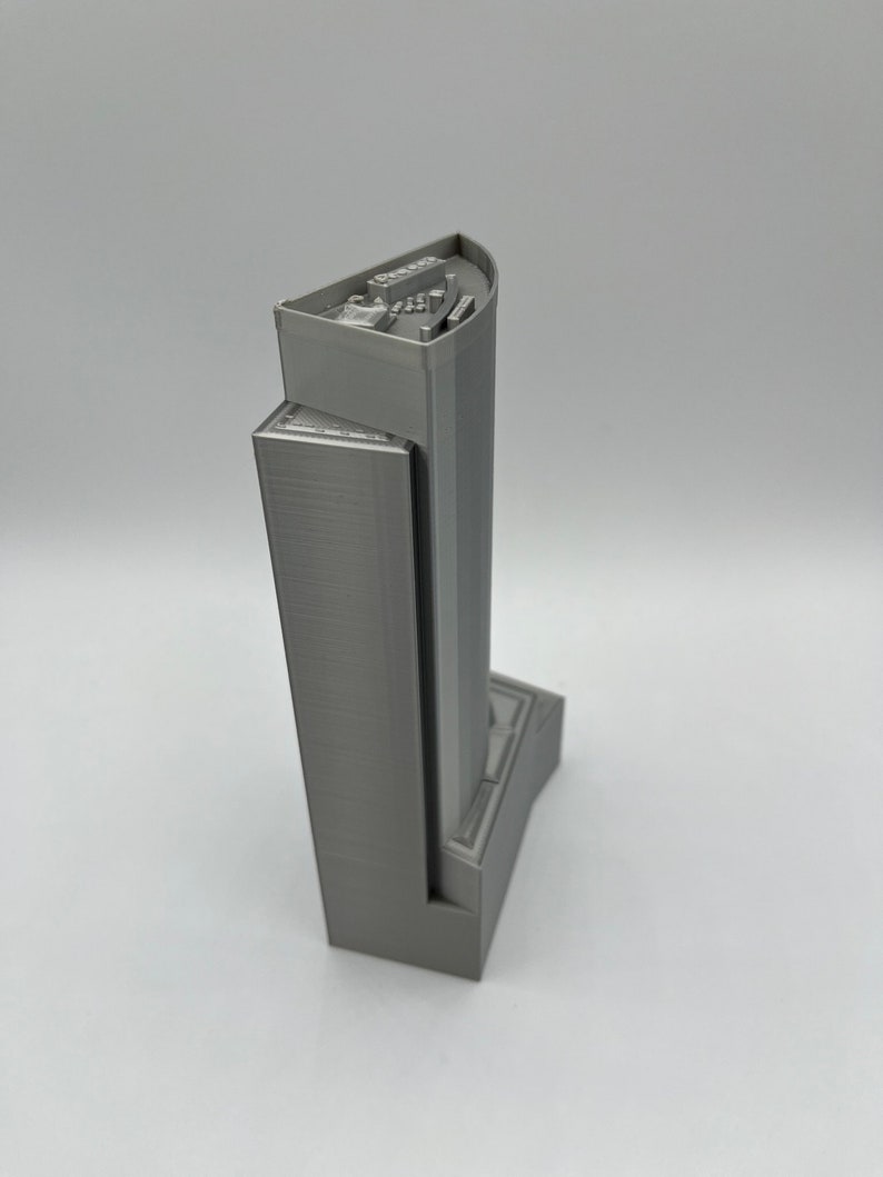 May include: A gray 3D printed model of a skyscraper with a detailed top and a base.
