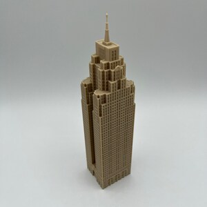 May include: A beige miniature model of a skyscraper with a pointed roof and many windows.